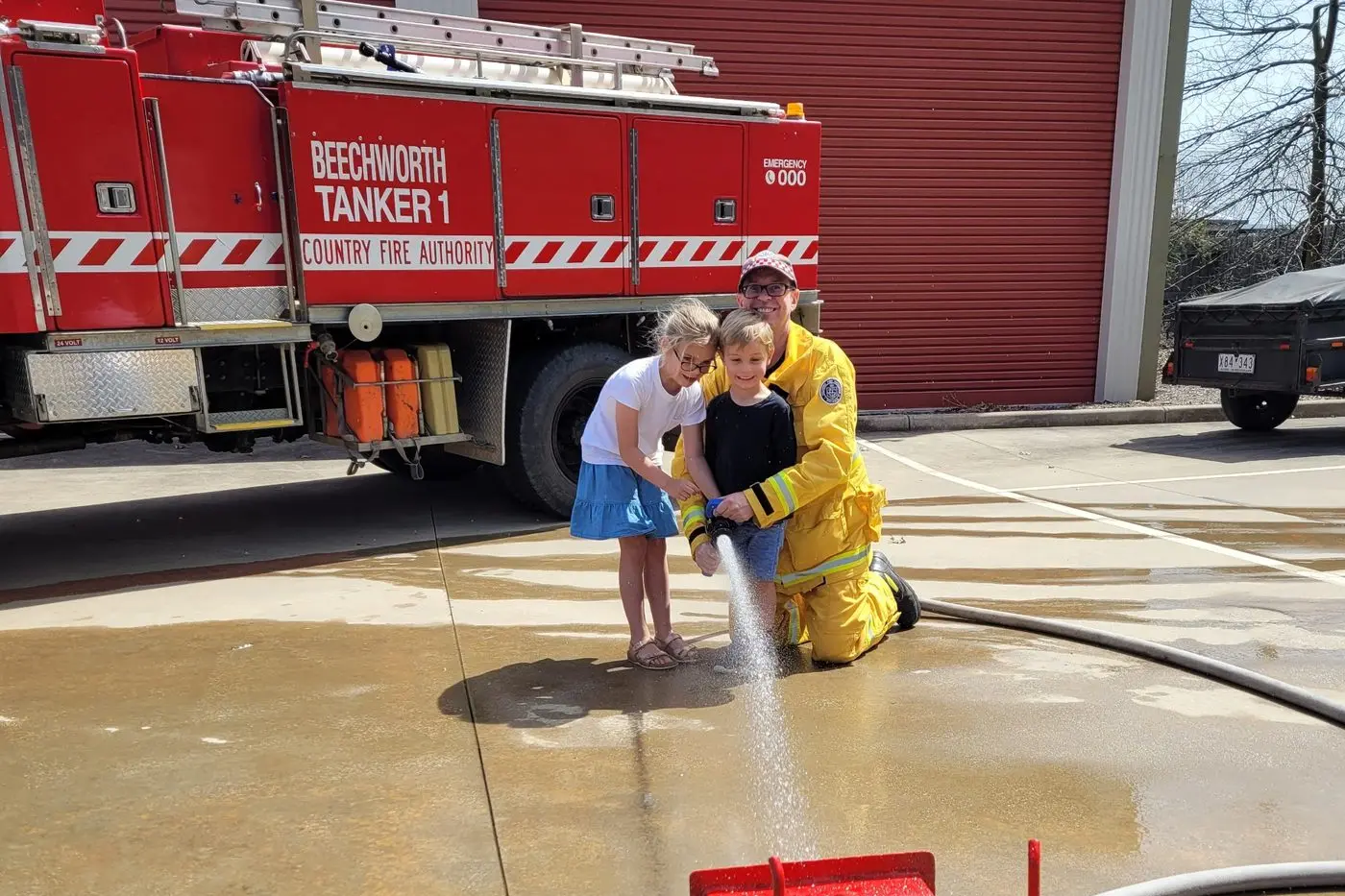FUN: Six-year-old Livija Makins with her three-year-old brother George with fire brigade volunteer Andrew Savvy showing the pair how to hose the new toy trucks down the hose line on Sunday. PHOTOS: Coral Cooksley